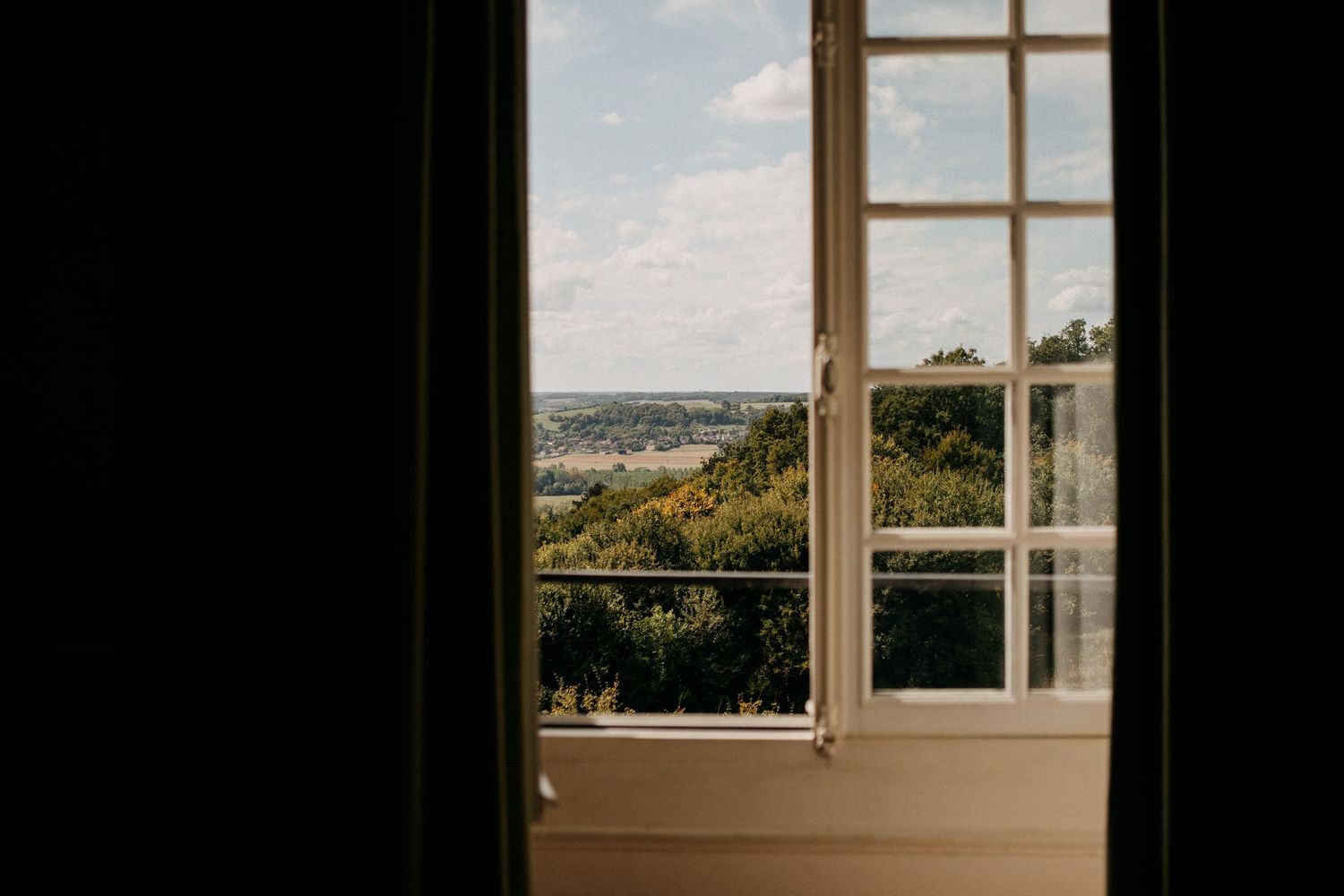 Bright French window opens to a scenic countryside view with lush green trees under a partly cloudy sky.