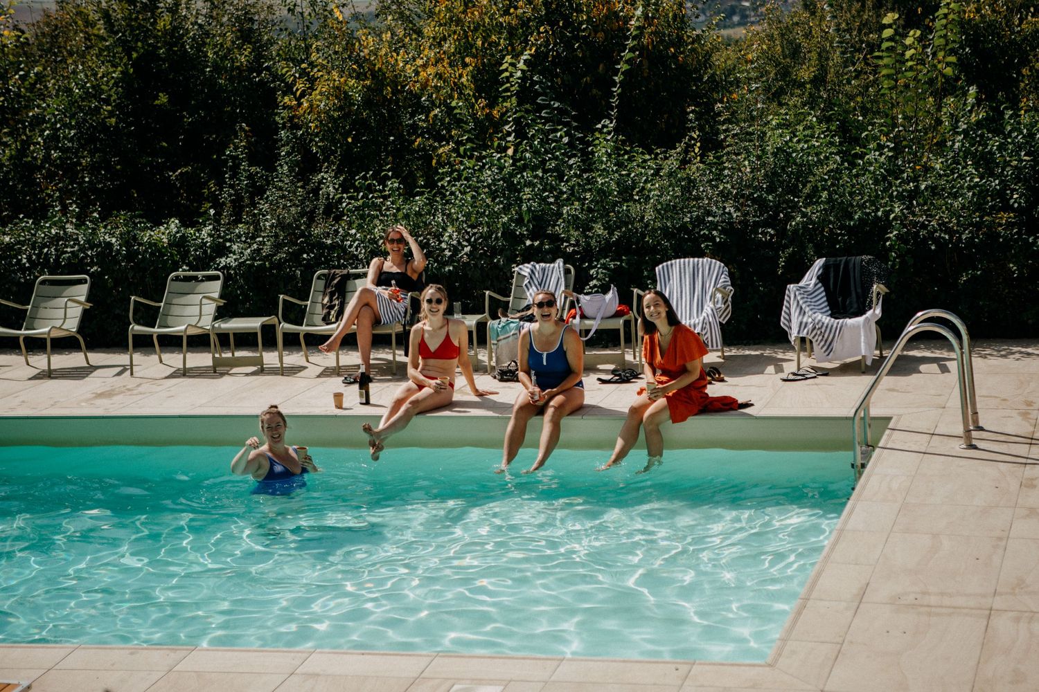 Group of women in colorful swimsuits relaxing by a sunny outdoor pool on a warm summer day.