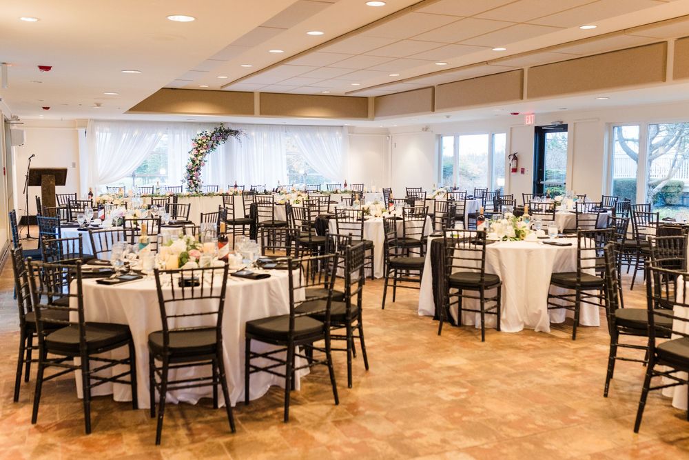 Elegant wedding reception venue with black chiavari chairs and round tables set up in a bright banquet room.