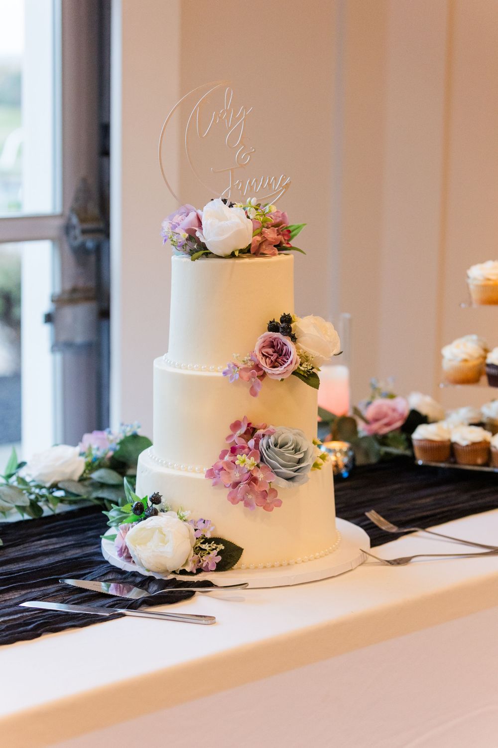 Row of white wedding cakes decorated with fresh flowers in shades of purple and pink displayed on a windowsill.