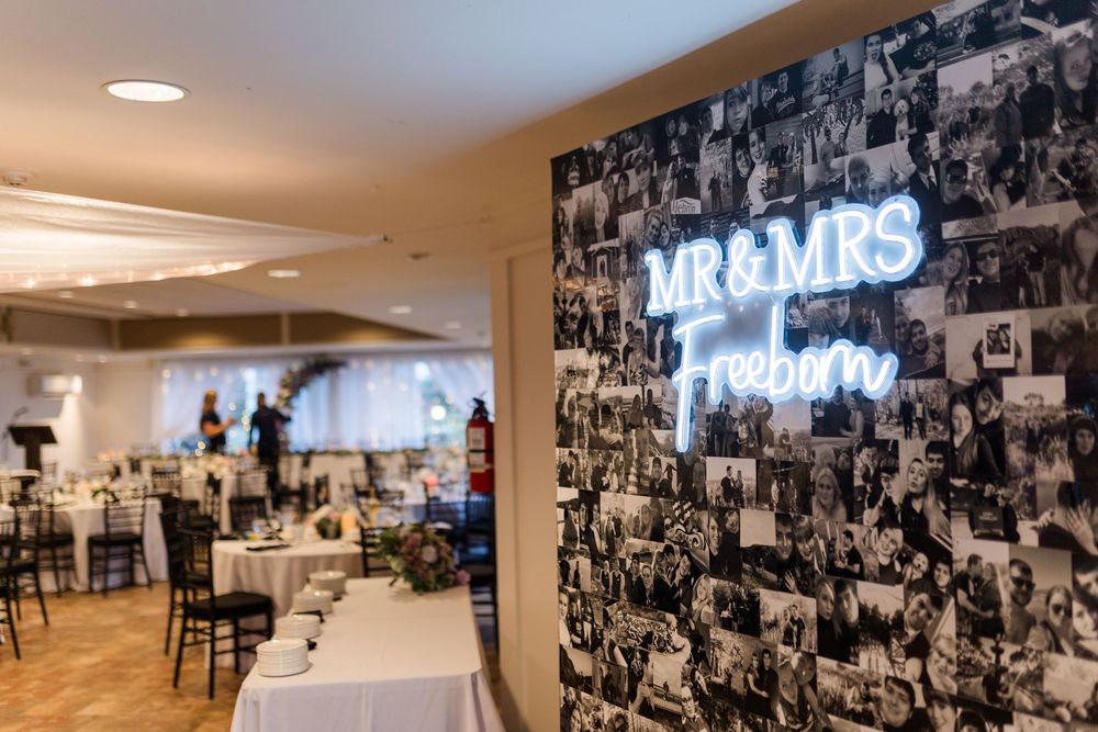 Illuminated neon 'MR & MRS' sign mounted on black and white photo collage wall in wedding reception venue.