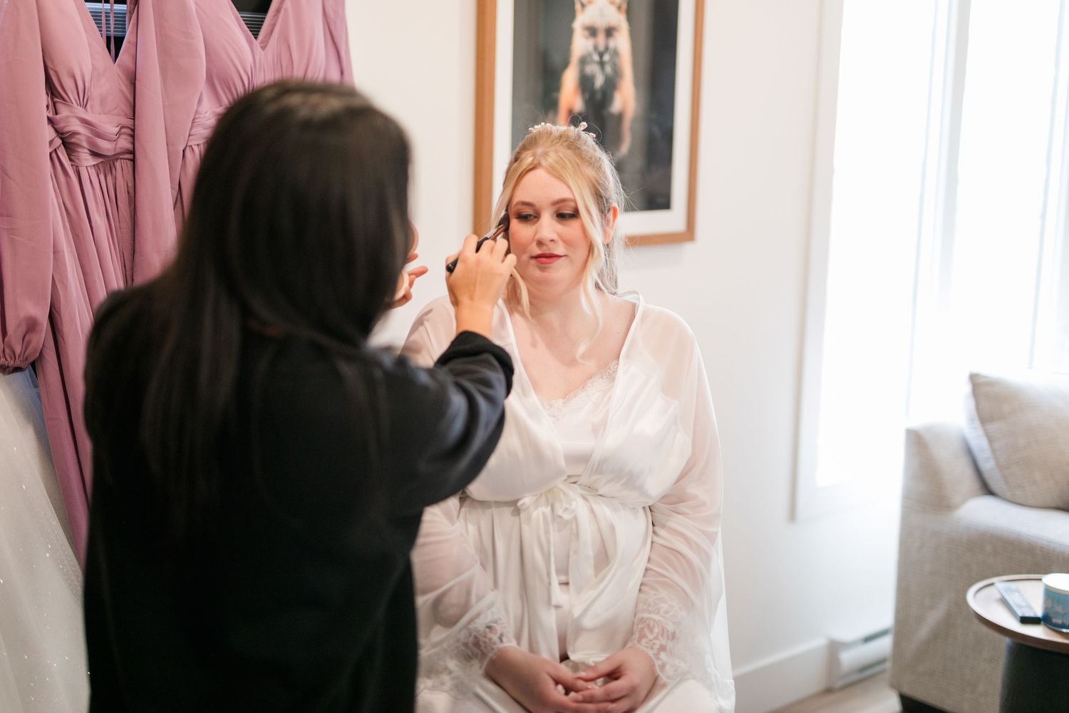 A bride getting ready on her wedding day in a soft pink room with natural light streaming through the windows.