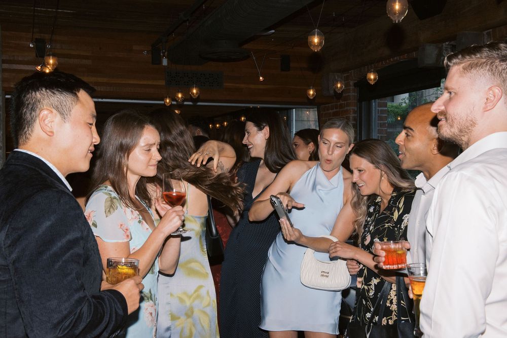 Party guests socializing and enjoying drinks at an indoor event with ambient lighting.