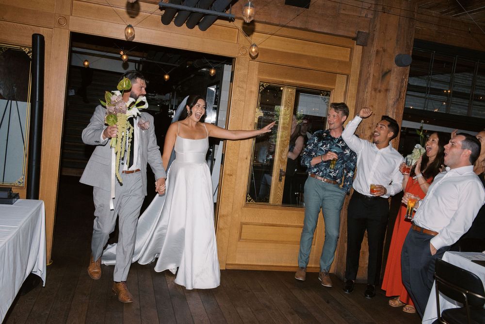Wedding guests dancing and celebrating on a rustic wooden dance floor at an indoor reception venue.