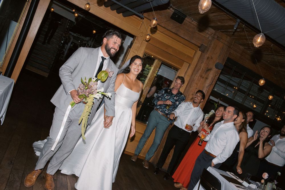 Wedding celebration scene in a rustic wooden venue with guests gathered around tables.