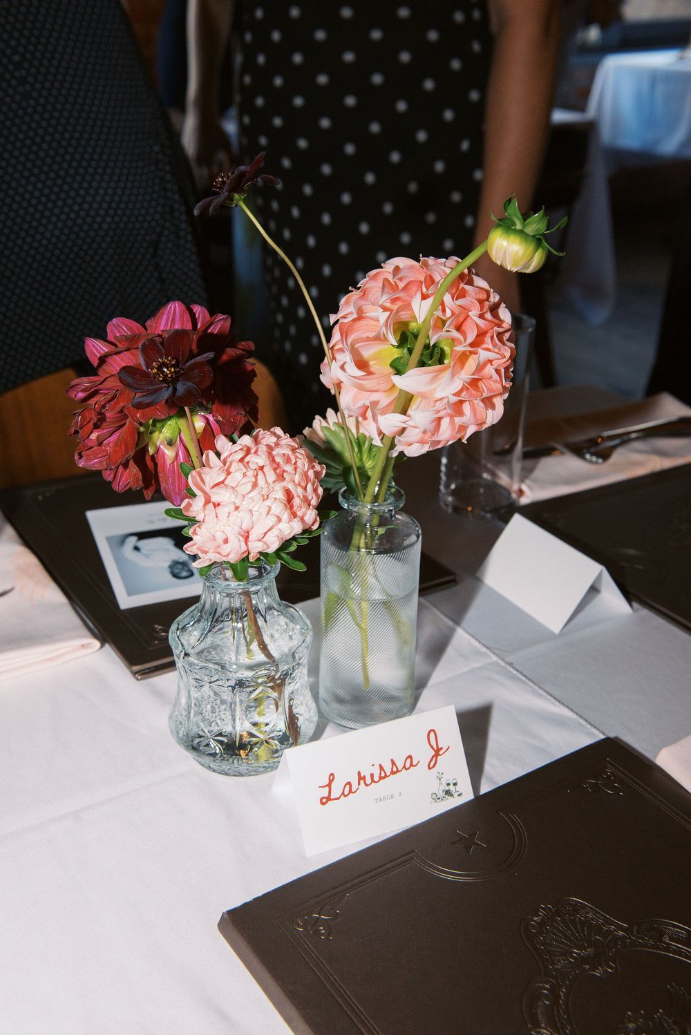 Pink and burgundy flowers in mason jars decorate a dark table with handwritten place cards.