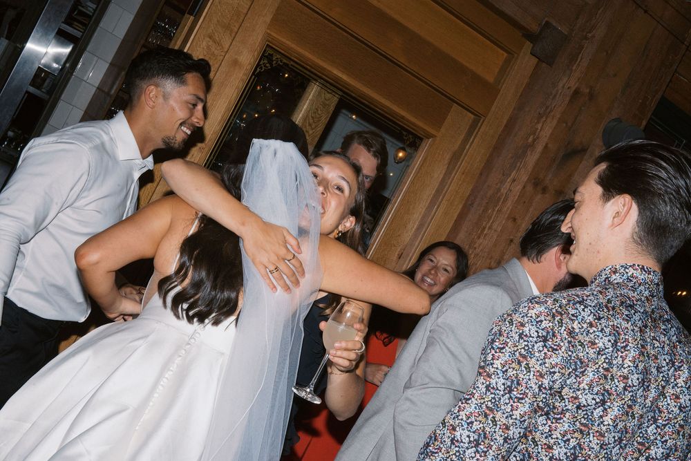 Couples dancing together at an indoor wedding reception with wooden beams and warm lighting.