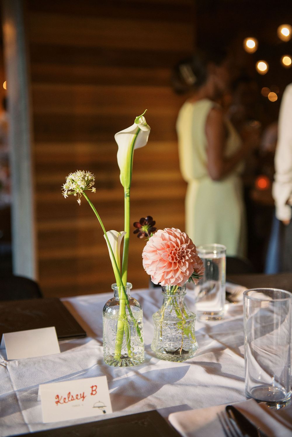 Elegant table settings with pink dahlias in bud vases and place cards at a wedding reception.