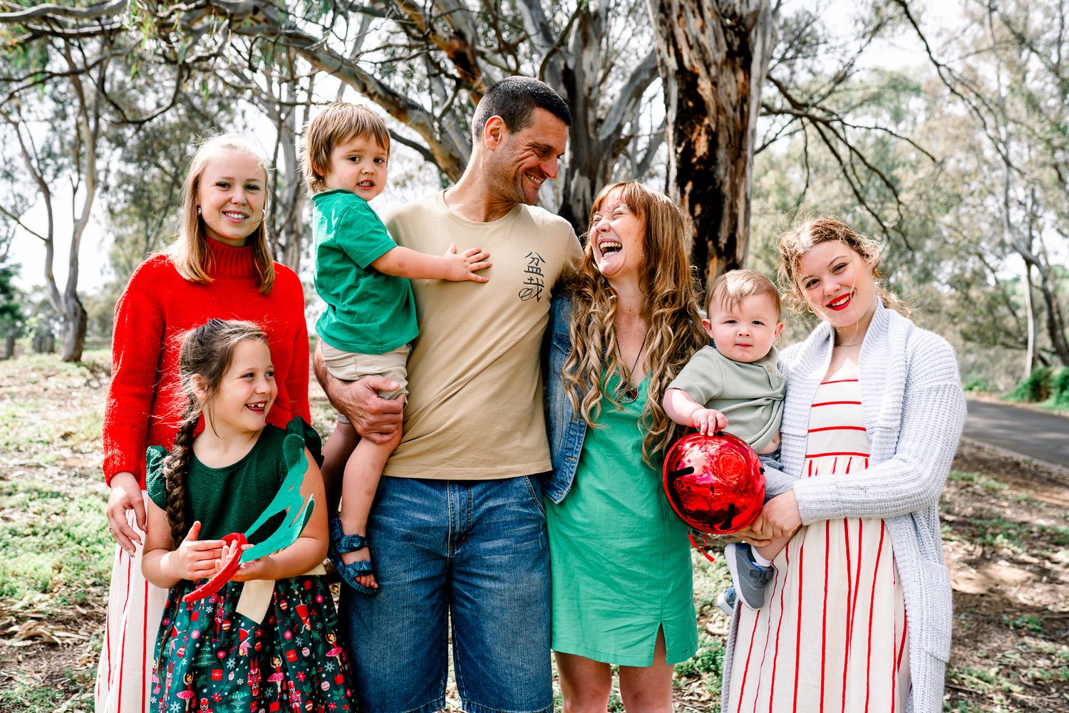 A family group shares joyful moments together outdoors in coordinated green and red outfits during a Melbourne Christmas Mini session.