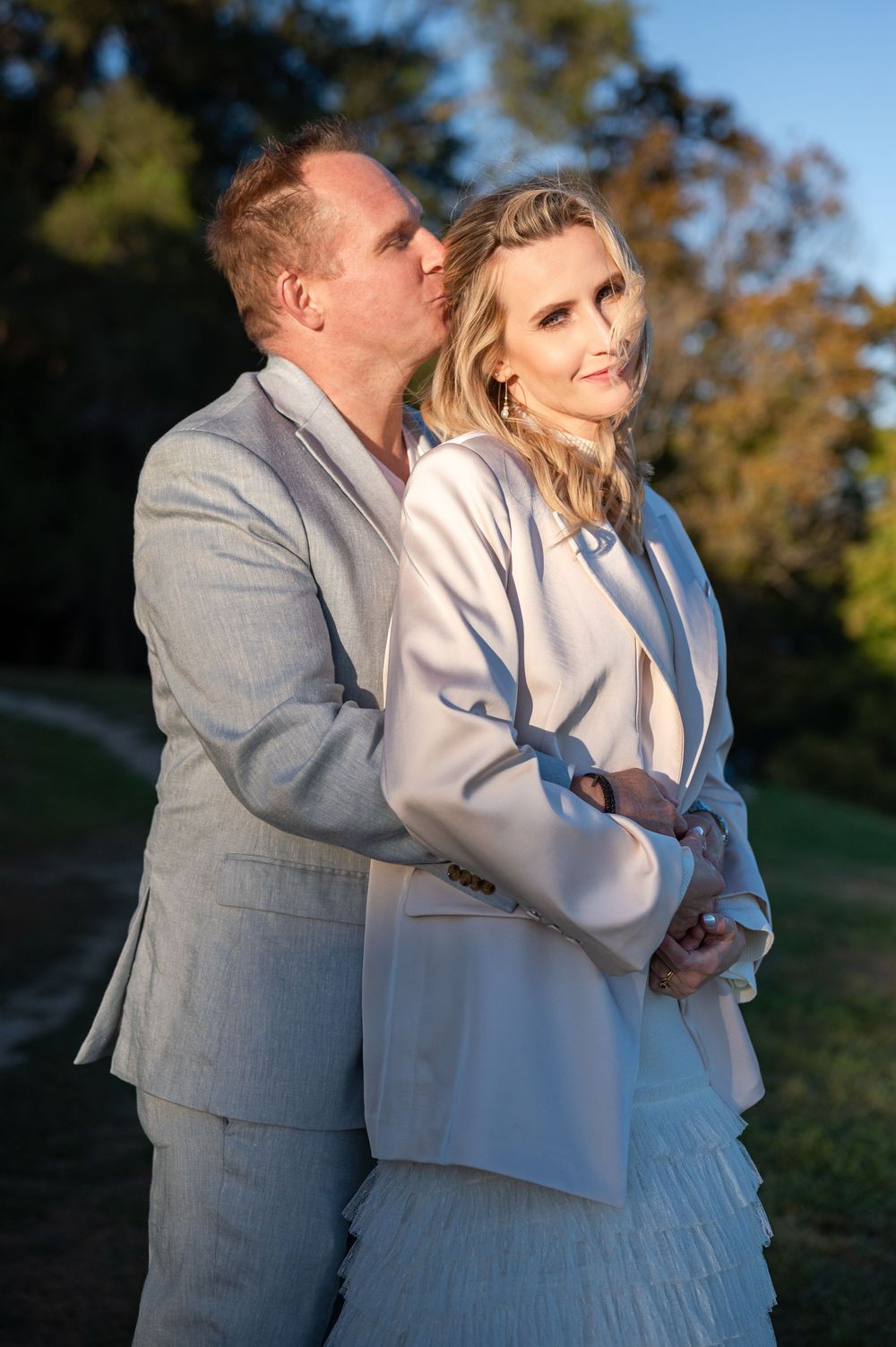 A couple embraces outdoors during a romantic photoshoot at sunset wearing coordinated gray and white outfits.