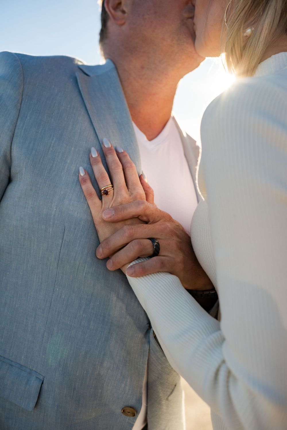 Close-up sequence of a couple embracing in formal attire with light gray suit and white dress against sunlit backdrop.