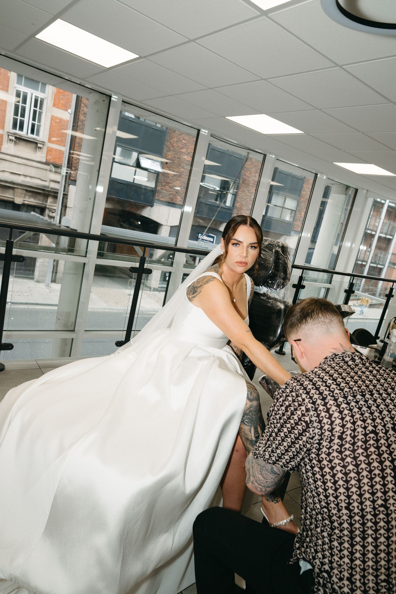 Behind-the-scenes photo of a photographer adjusting a flowing white wedding dress in a bright studio space.
