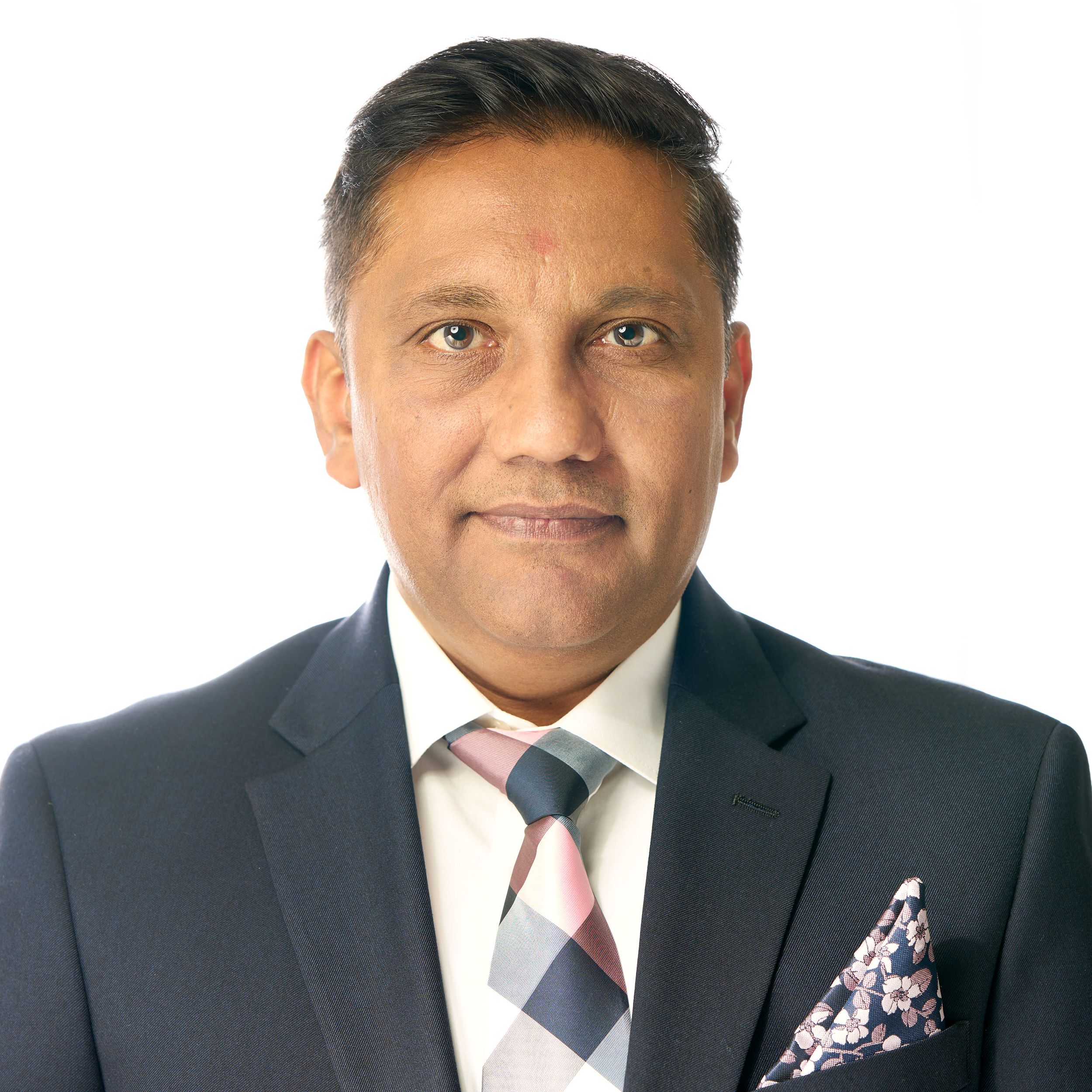 Professional headshot of someone in a dark business suit and patterned pocket square smiling warmly at the camera.