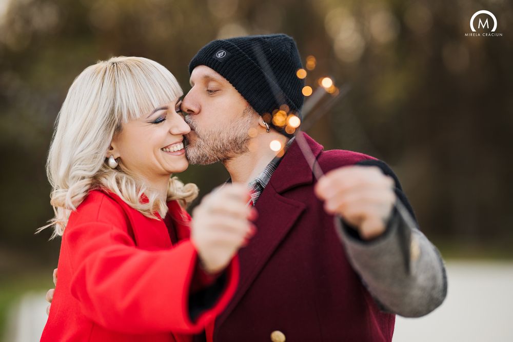 A couple in a red coat shares a romantic moment while taking selfies outdoors during autumn.