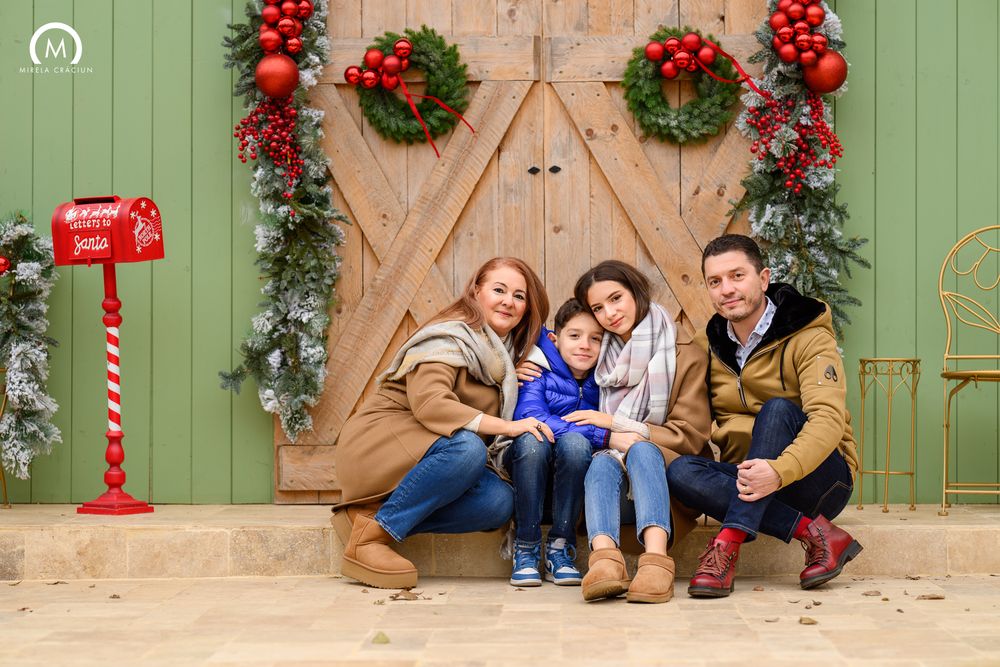 Four festive holiday photos show people sitting against a green barn door decorated with Christmas wreaths and garland.