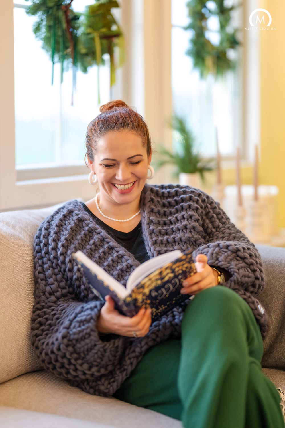 Person relaxing on a couch with a cozy chunky knit blanket while reading a book in a sunlit room.