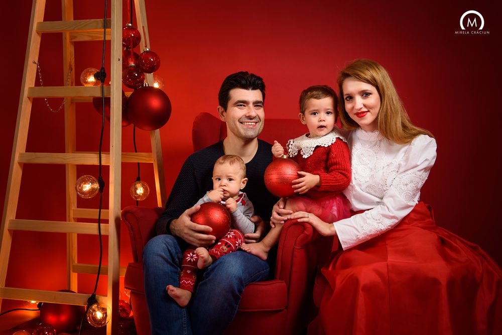A family in red and navy outfits poses together for Christmas photos with a wooden ladder and ornament decorations.