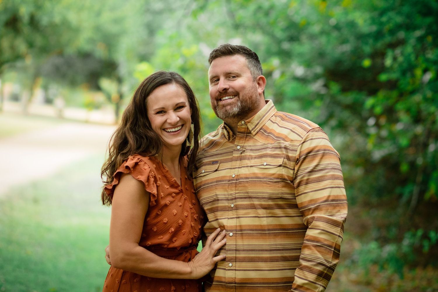 A couple shares a tender embrace while standing together in a lush green outdoor setting during a family mini session at Mills Pond Park