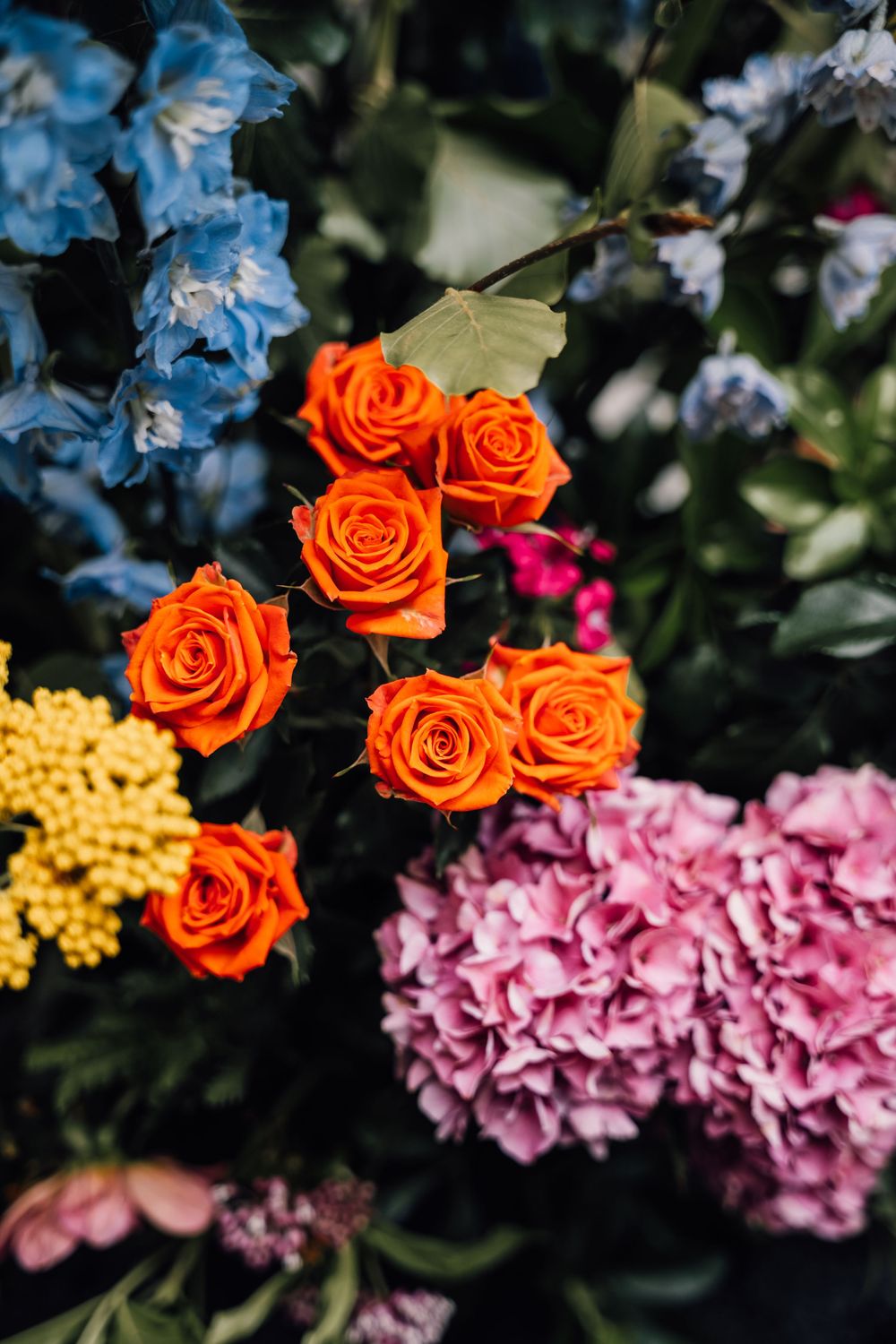 Vibrant floral arrangement featuring orange roses, blue hydrangeas, and pink blooms.