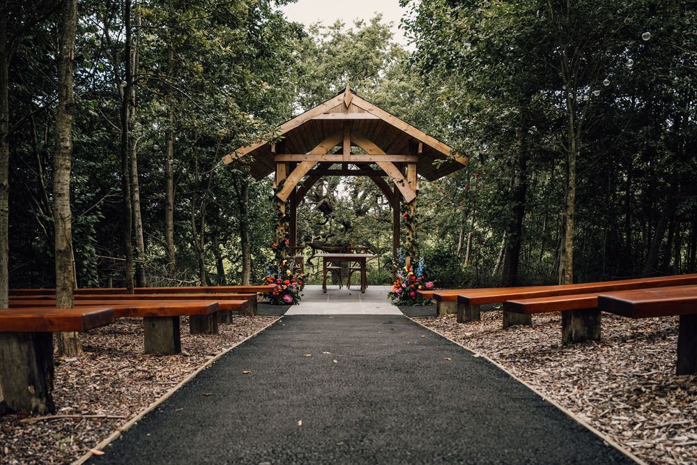 Long wooden pavilion structure with exposed beams set in a wooded area.