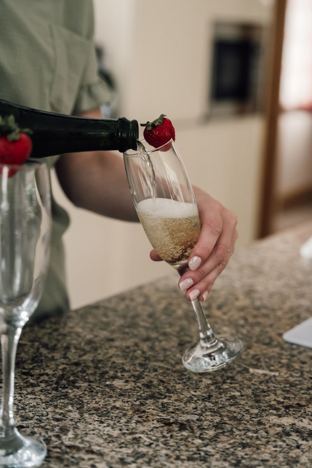 Wine glasses being filled on a granite countertop with red rose garnish.