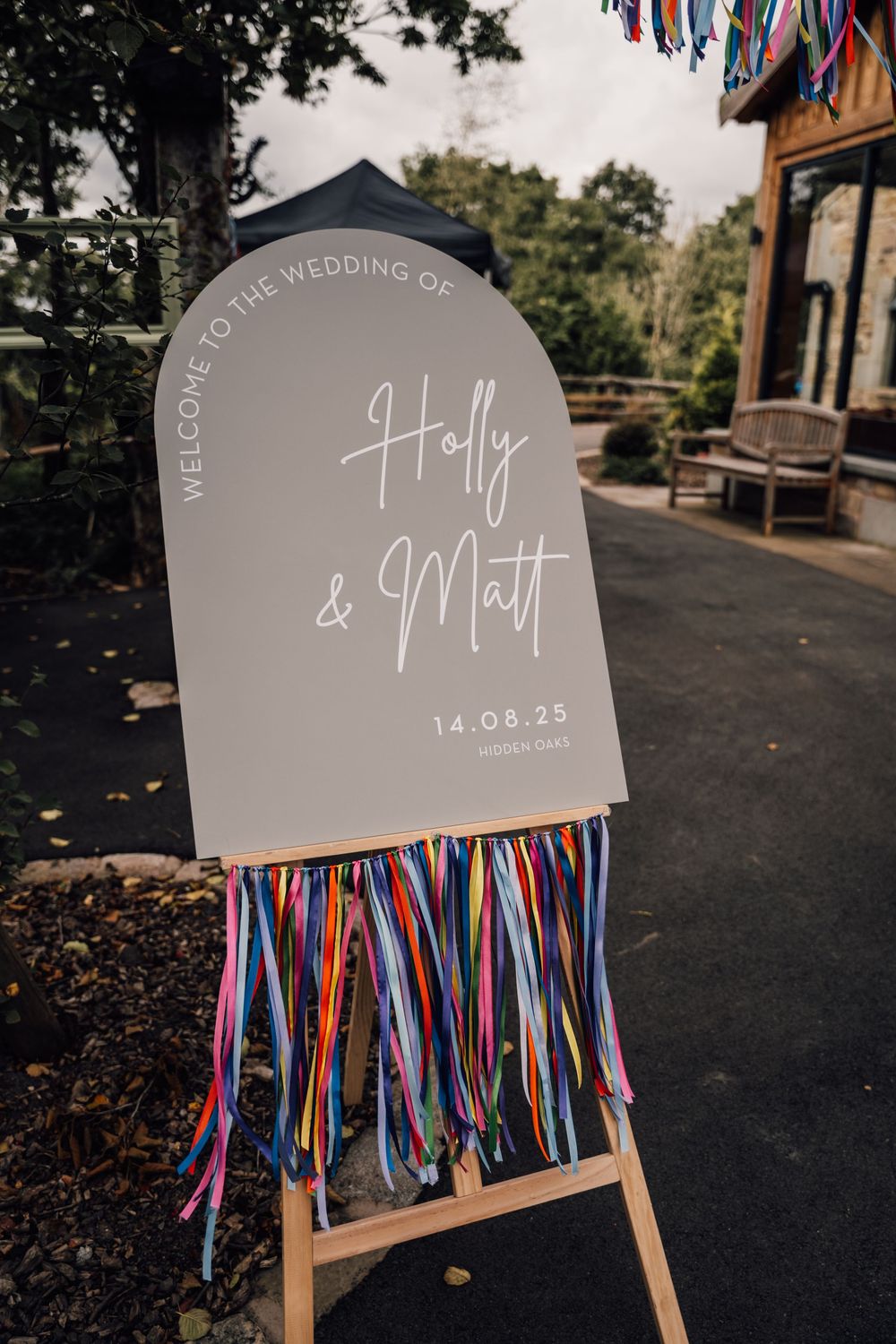 Wedding welcome sign with colorful ribbon streamers on a gray curved board.