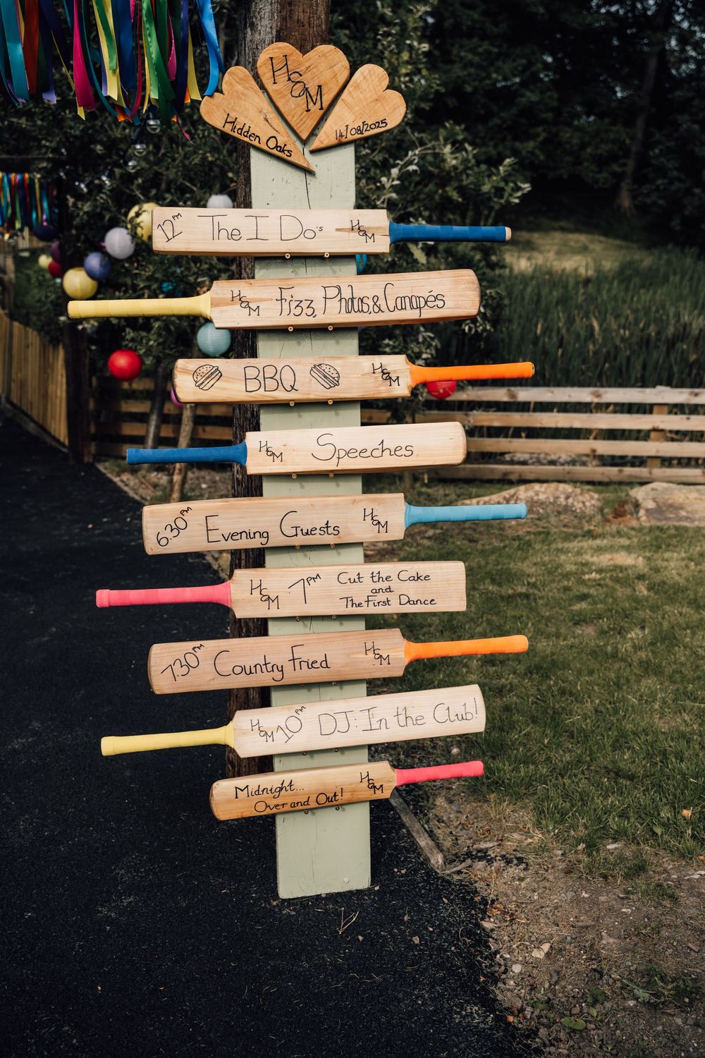 Rustic wooden directional signs with colorful ribbons displaying wedding event details.