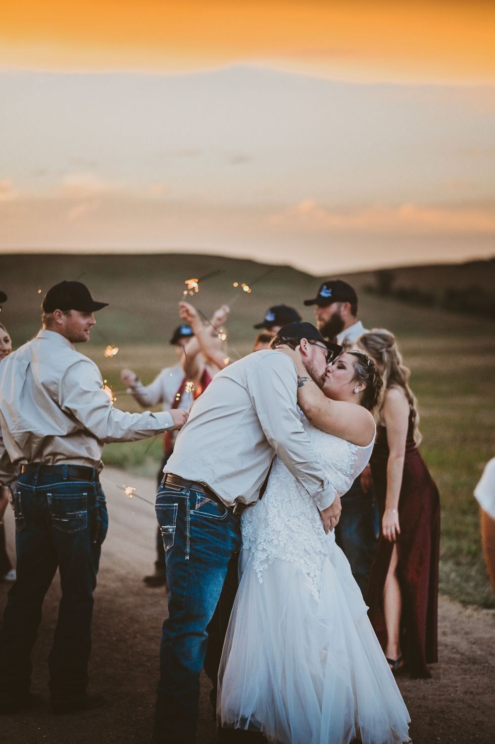 Wedding party takes celebratory shots at sunset against rolling hills landscape during outdoor reception.