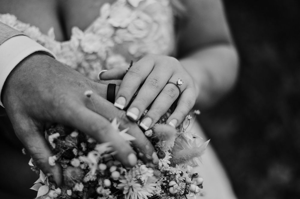 Black and white image showing hands holding small white flowers and petals in a delicate arrangement.