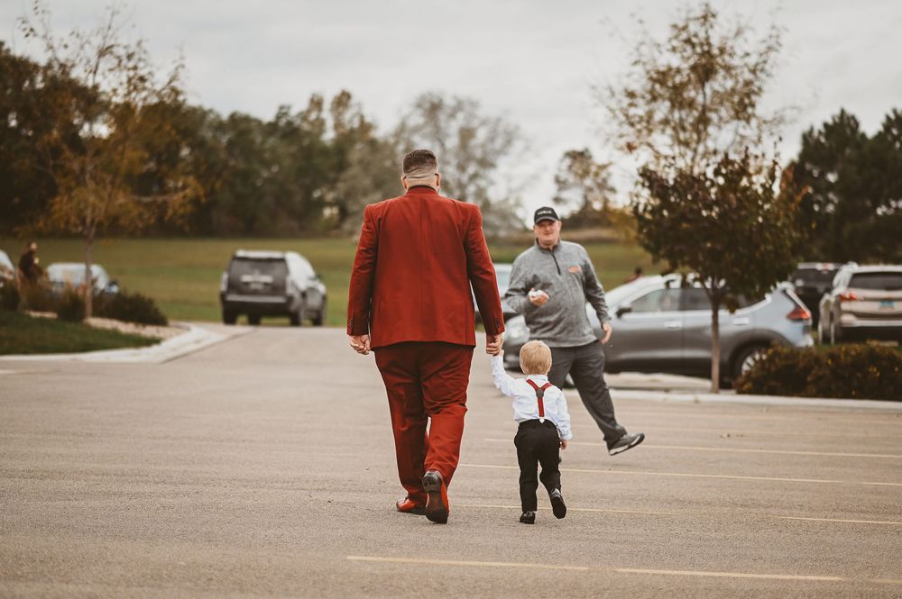A person in a red coat walks with a child across a parking lot on an autumn day.