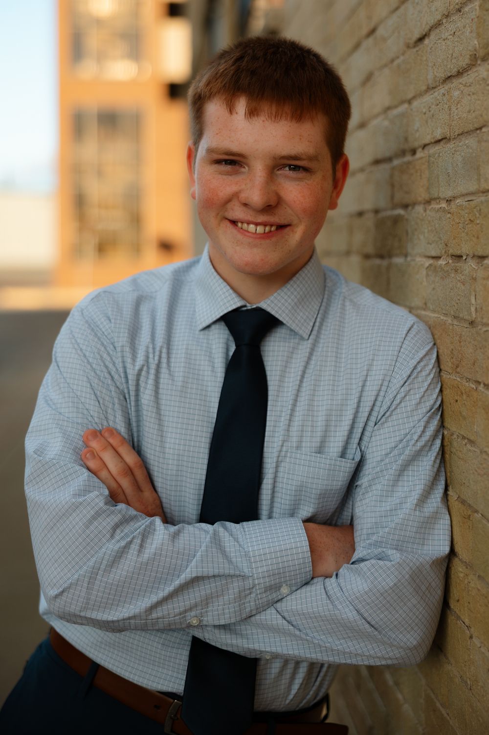 A student in a light blue dress shirt and navy tie poses confidently against a brick wall in a series of portraits.