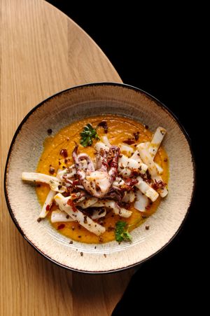 Artfully plated seafood dish with white fish and garnishes on a rustic ceramic plate.