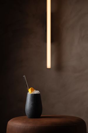 A modern cocktail served in a black ceramic vessel with dramatic overhead lighting against a dark background.