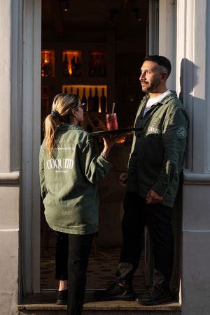People wearing matching green jackets gather near glass windows in evening light.