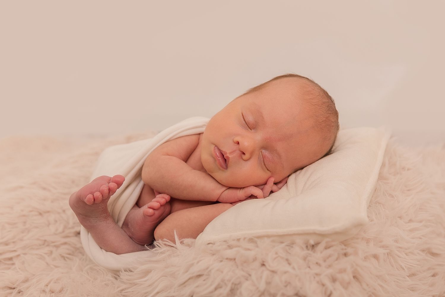 Sleeping newborn wrapped in soft blanket on textured beige backdrop. Photographer. Hull. East Yorkshire.