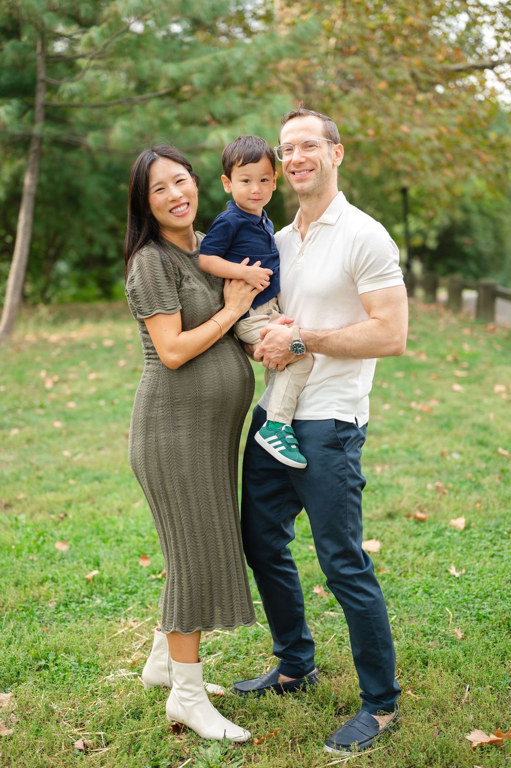 A family enjoys a playful moment together on grassy autumn ground with fallen leaves scattered around them in Central Park.