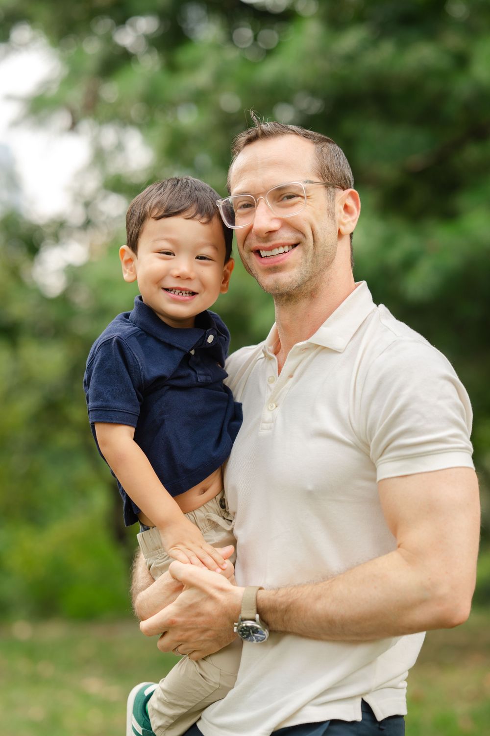 A child and his father share warm embraces and laughter during a playful moment in Central Park during a family photoshoot.