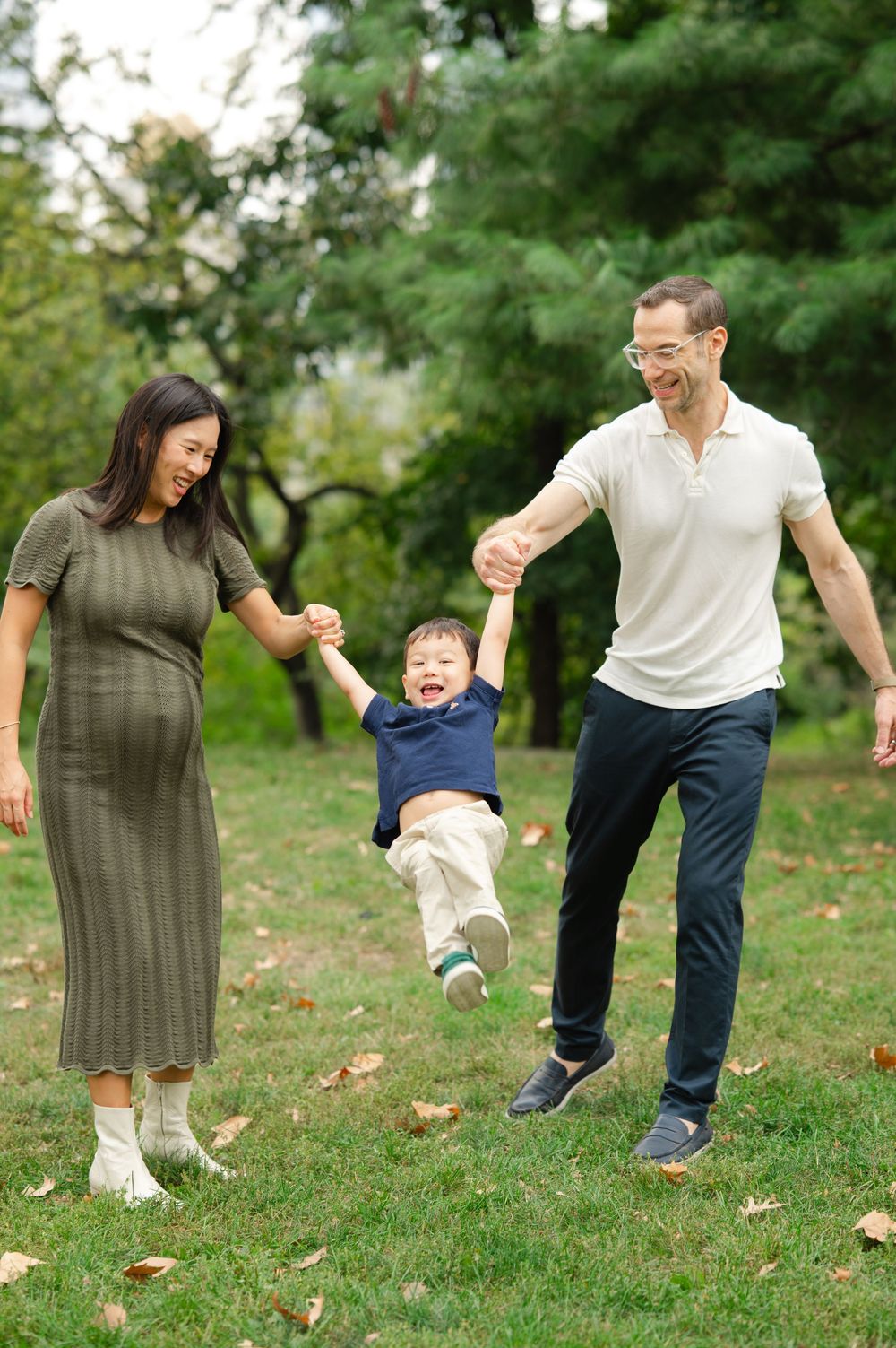 Family plays together on grassy hillside during outdoor autumn photo session in Central Park.
