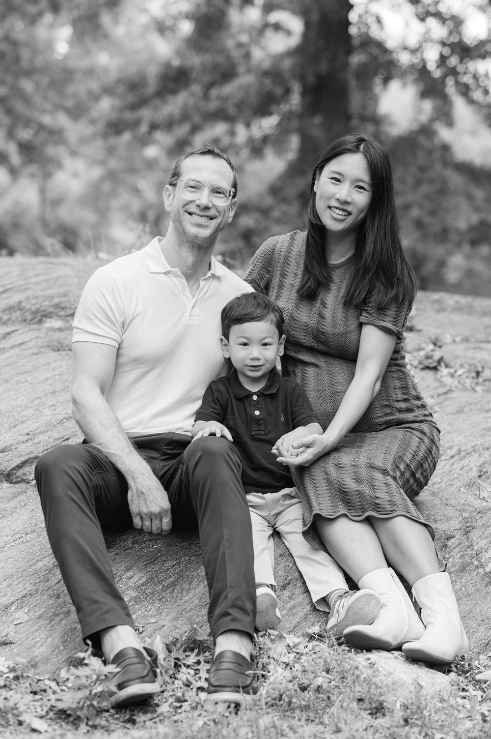 Black and white family portrait series showing intimate moments sitting together on a rocky outdoor surface.