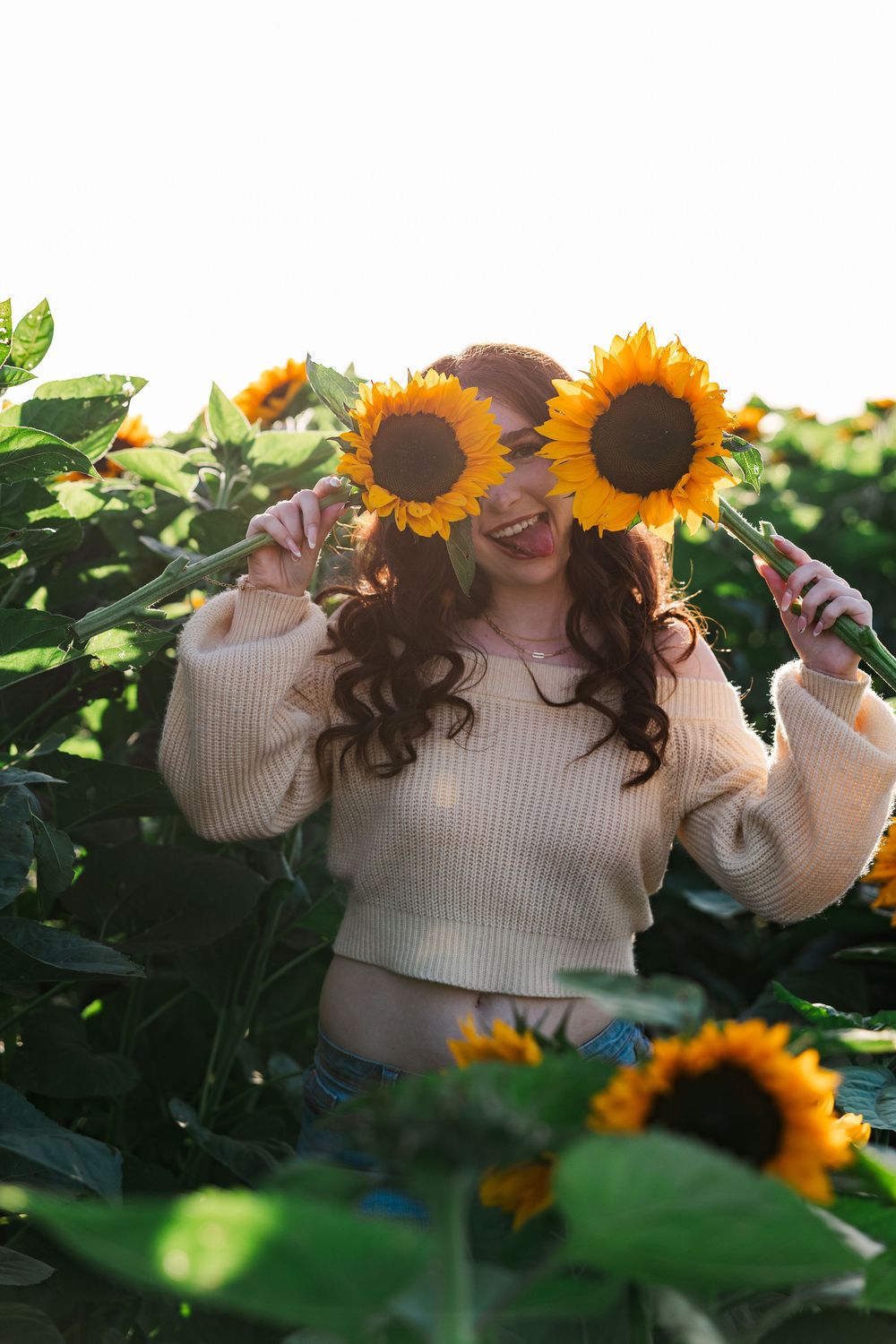 A playful moment in a sunflower field with someone holding bright yellow blooms in front of their face.