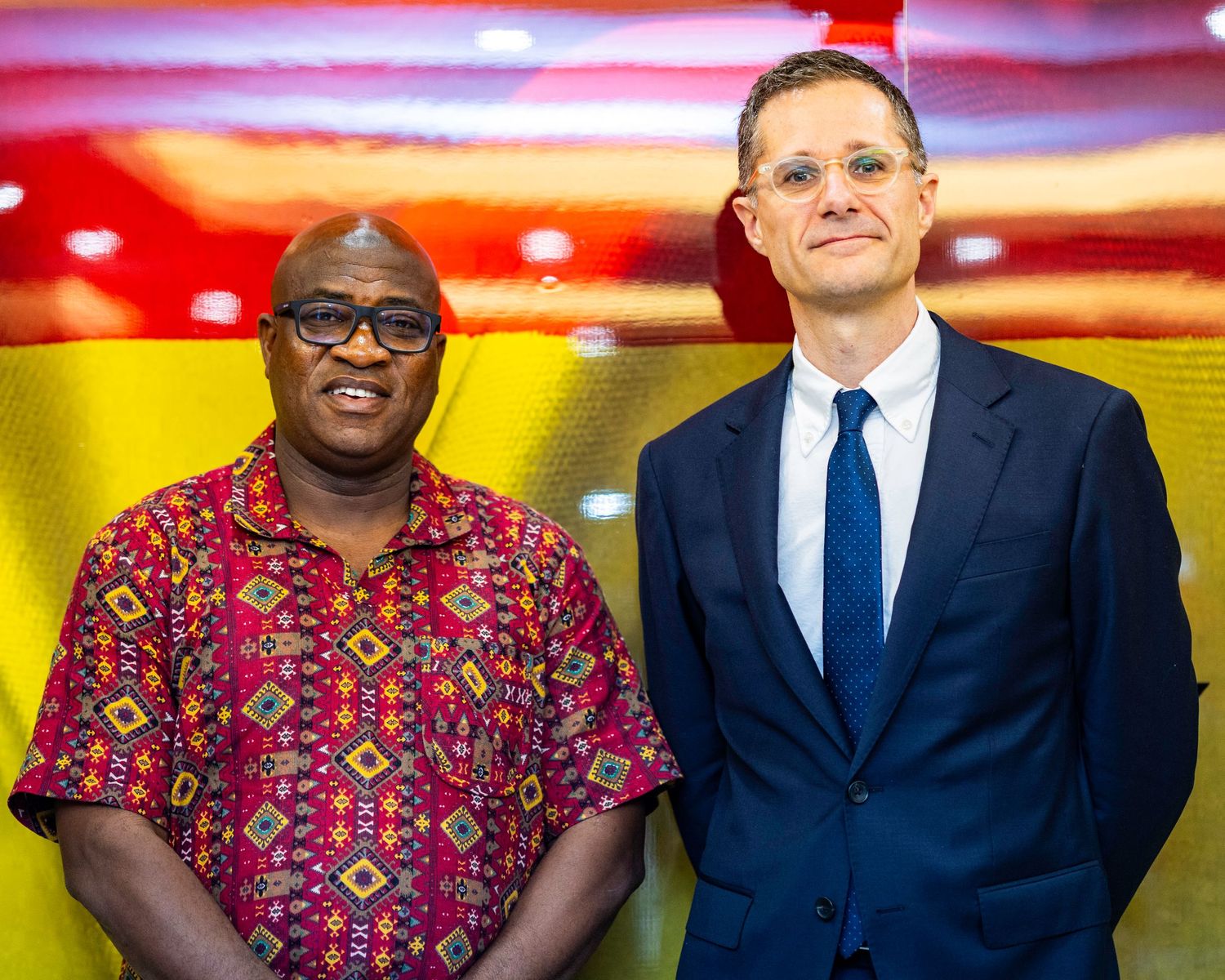 Two professionals, one in traditional African print and one in suit, standing together at formal event.