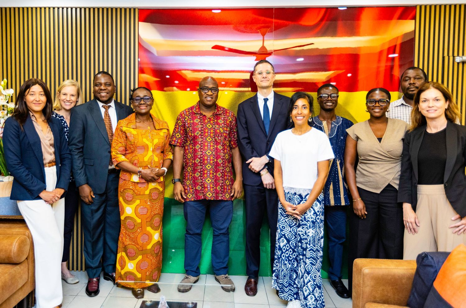 Group photo of diverse professionals in business attire standing against decorative red-lit wall.