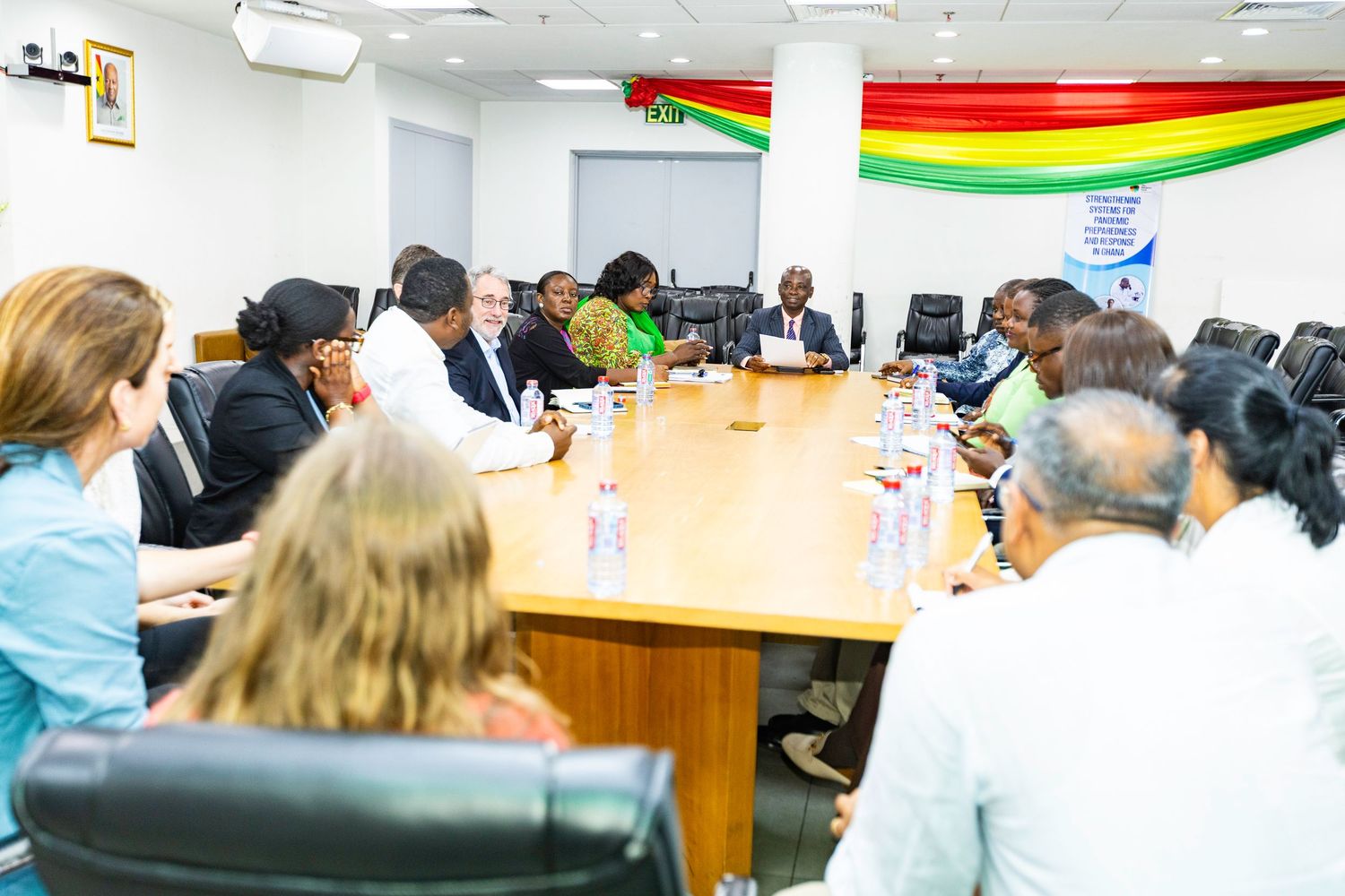 Wide view of business meeting in conference room with Ghana flag decorations and professional setup.