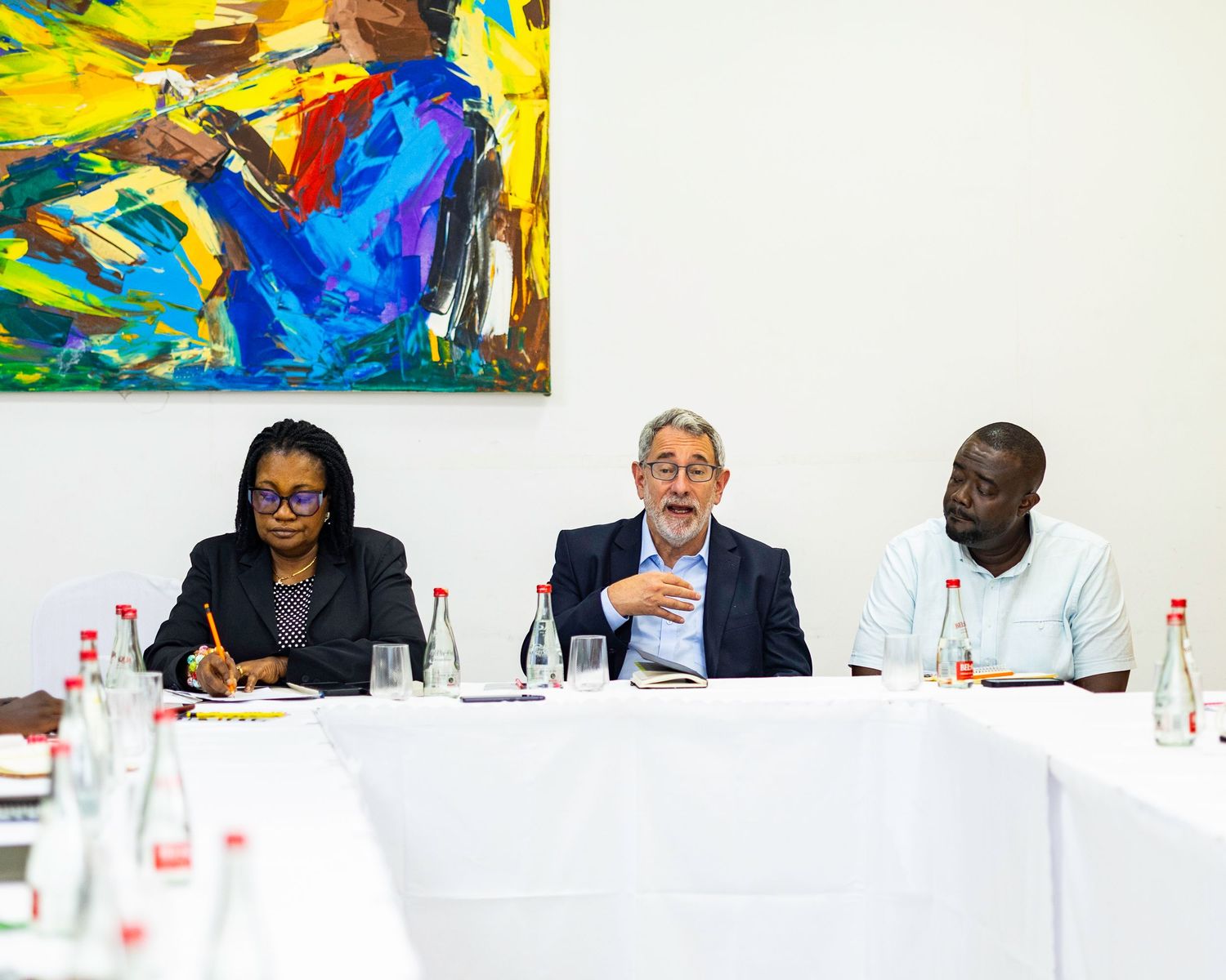 Business meeting with participants seated at white table with colorful artwork on wall.