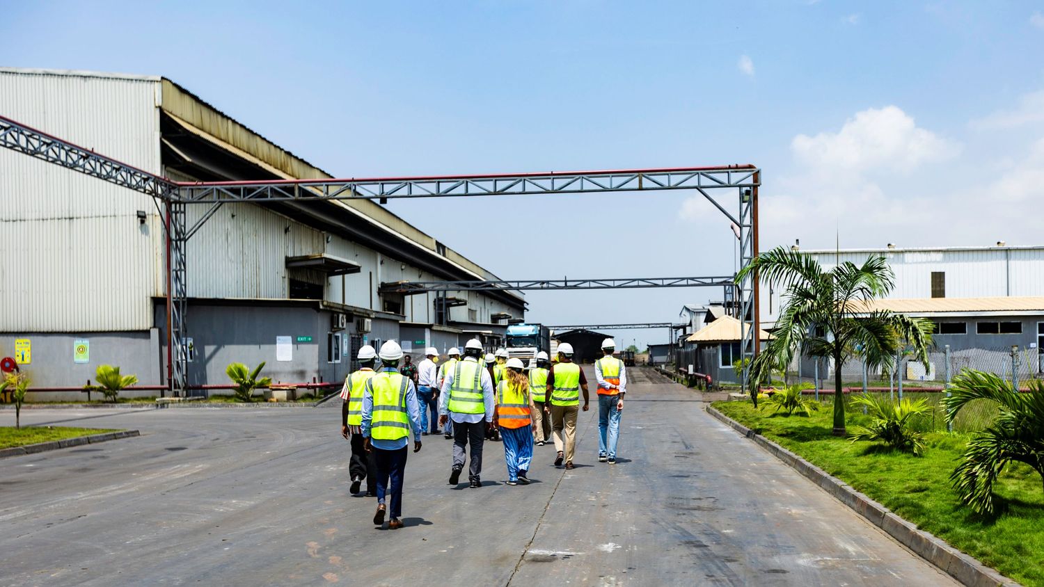 Industrial workers in safety vests walking through a warehouse facility with overhead metal structures.