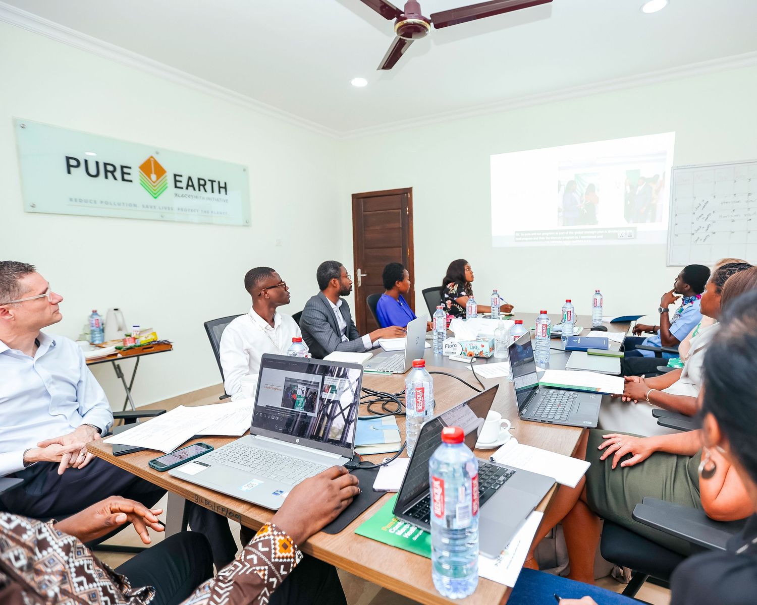 Business team meeting in conference room with Pure Earth banner and laptops.