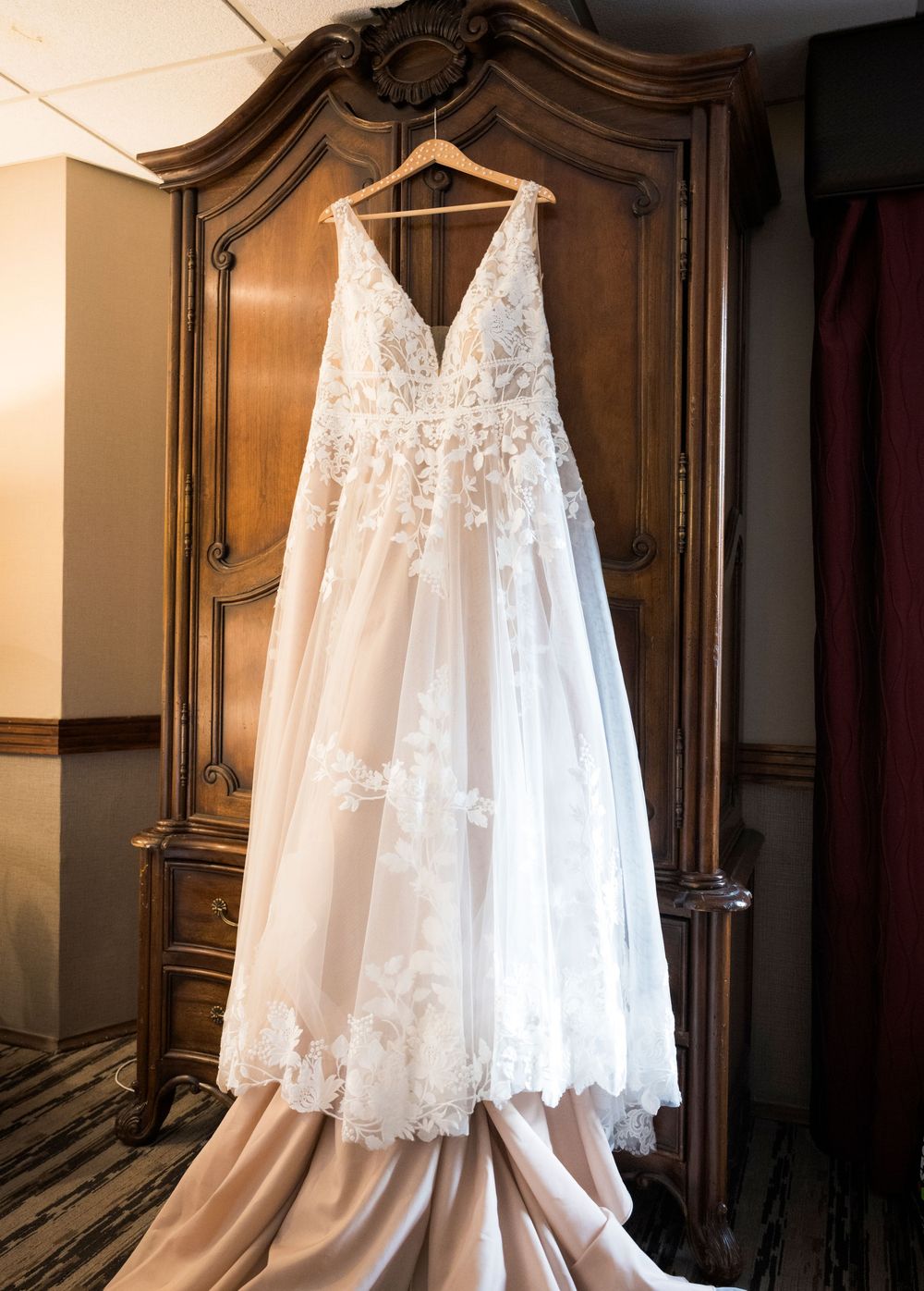 Elegant white lace wedding dress with delicate details hanging in a classic wooden wardrobe.
