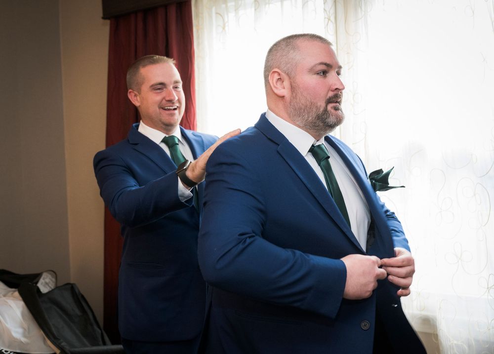 Wedding party members share candid moments in formal attire inside a venue.