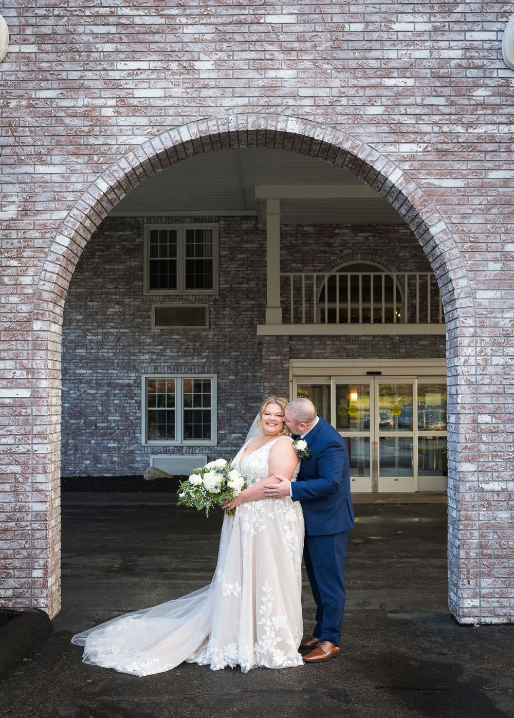 A romantic wedding couple poses under brick archways at their venue.