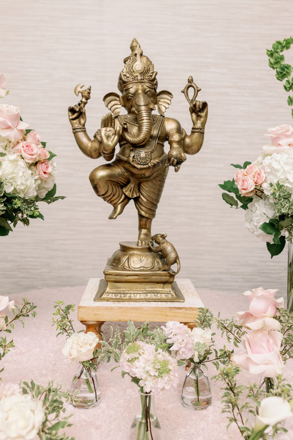 Bronze Ganesha statue displayed among pink roses and white floral arrangements.